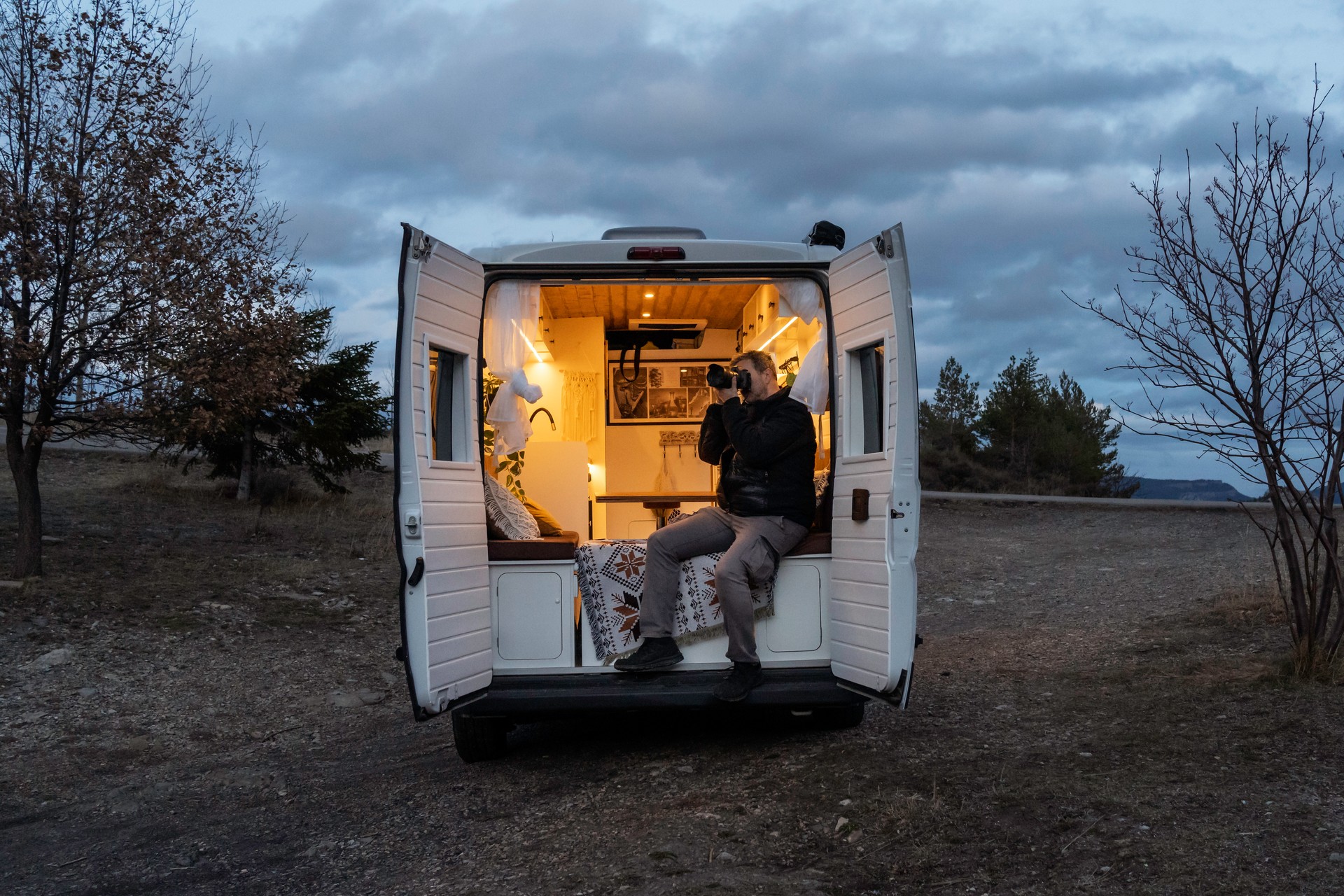 Mature man taking photos from the back of his camper van during sunset